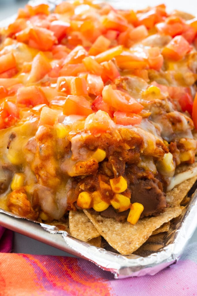 closeup of nachos with refried beans, cheese, corn and tomatoes on them.