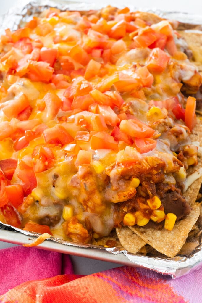 melted cheese and beans on nachos with corn and tomatoes.