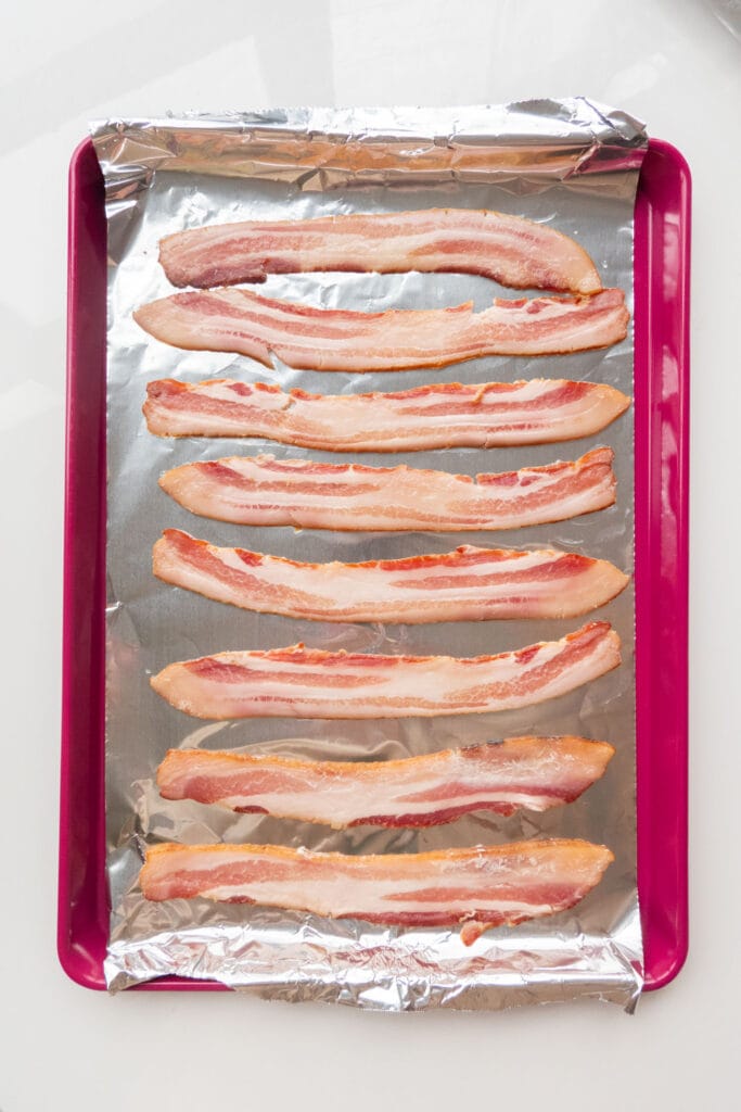 uncooked bacon on baking sheet.