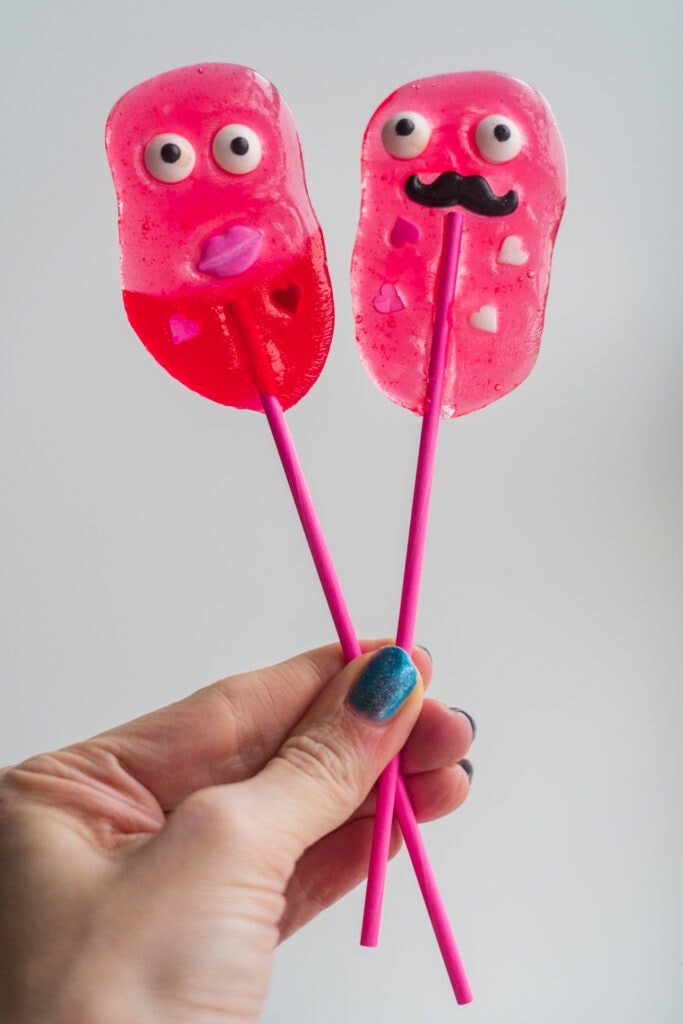 hand holding up 2 monster lollipops with faces on them.