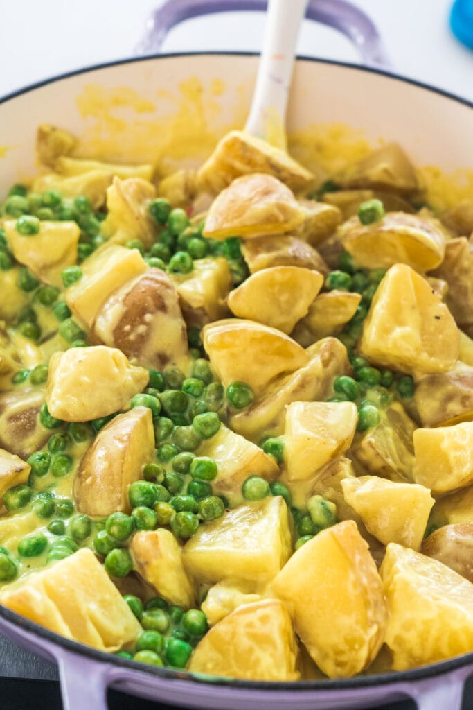 creamy potatoes and peas in skillet with spoon ready to serve.