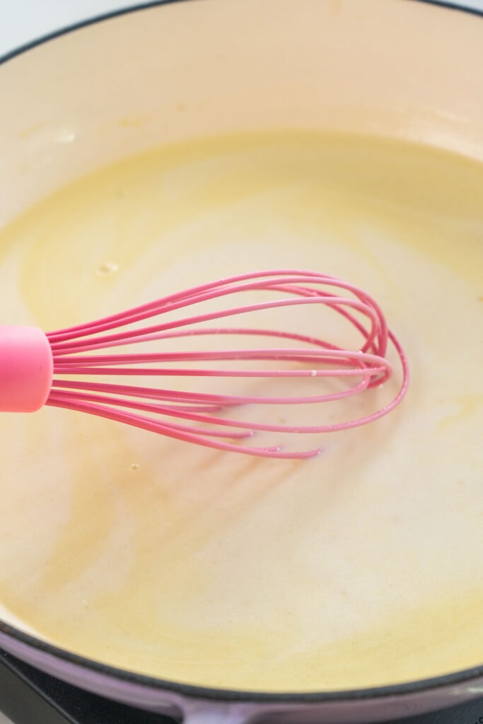 cream sauce being whisked by pink whisk in skillet.