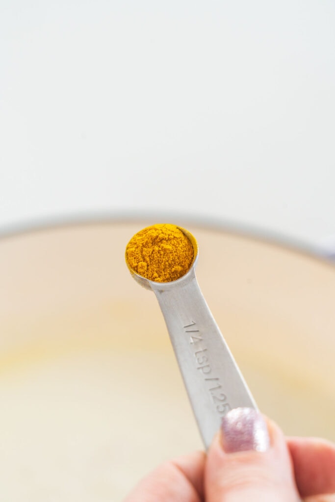 Measuring spoon filled with turmeric being added to skillet.