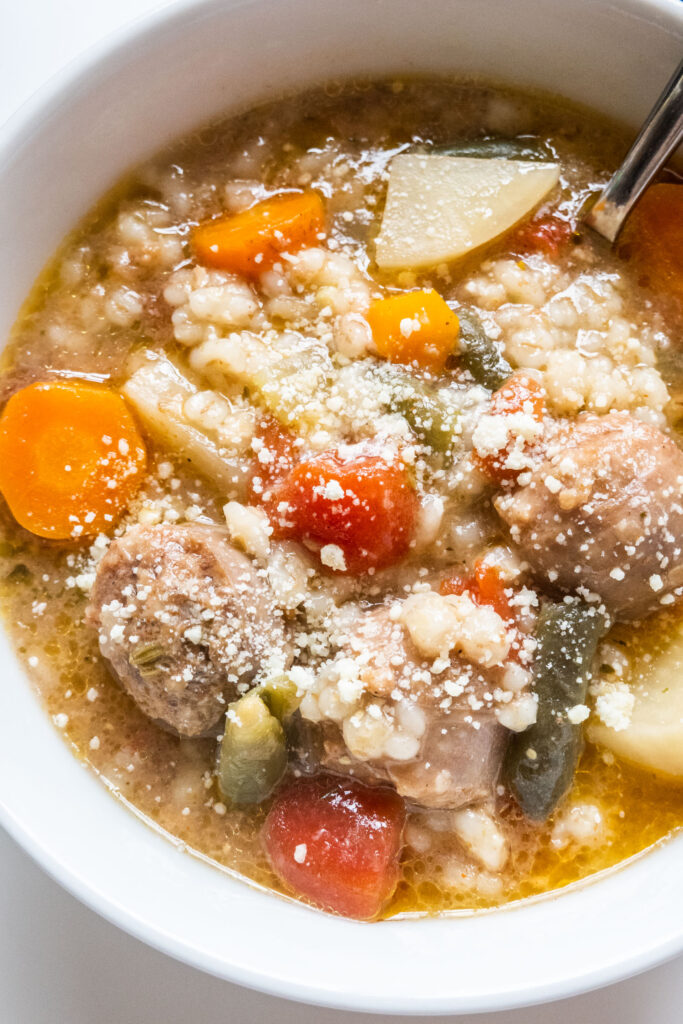 barley sausage soup in white bowl, with Parmesan cheese sprinkled on top.