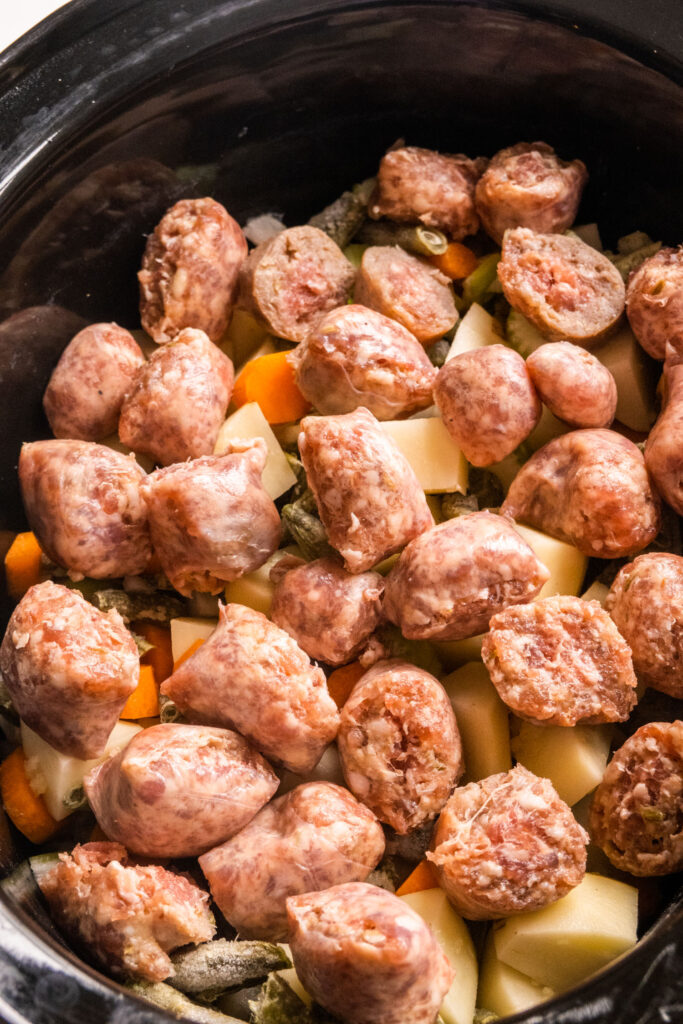 sausage added on top of vegetables in crockpot.