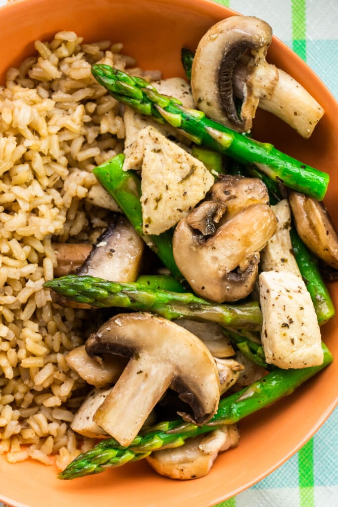 closeup of asparagus and chicken with brown rice in orange bowl.