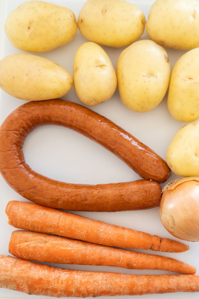 potatoes, kielbasa, carrots and onion on table.
