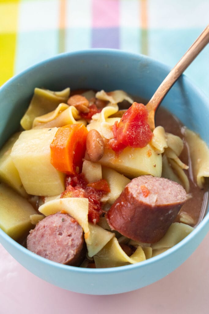 kielbasa soup in blue bowl on colorful table cloth. 