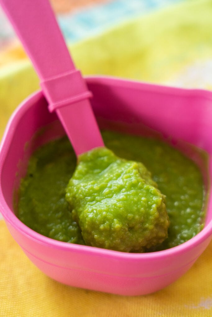 small pink bowl with pea puree on pink spoon.