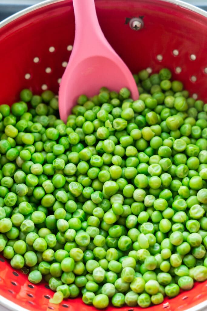 peas drained in strainer with pink spoon. 