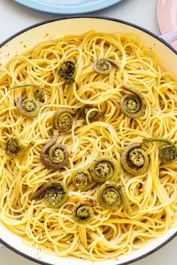 spaghetti and fiddleheads in skillet on table.
