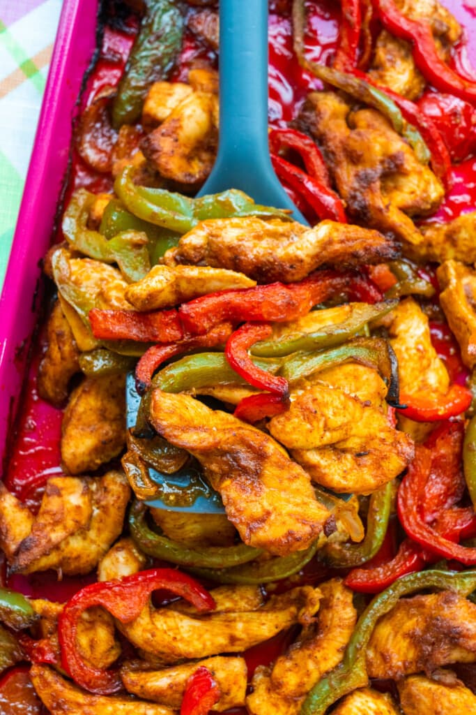 chicken and peppers being picked up by spatula on pink baking sheet.