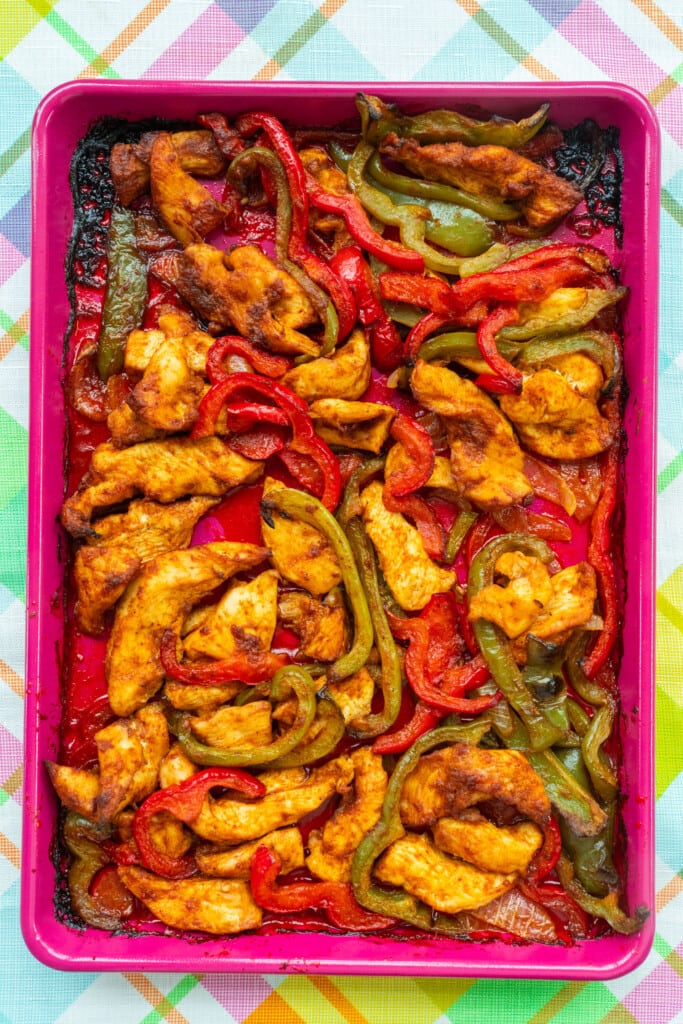 baked chicken and peppers on pink baking sheet.
