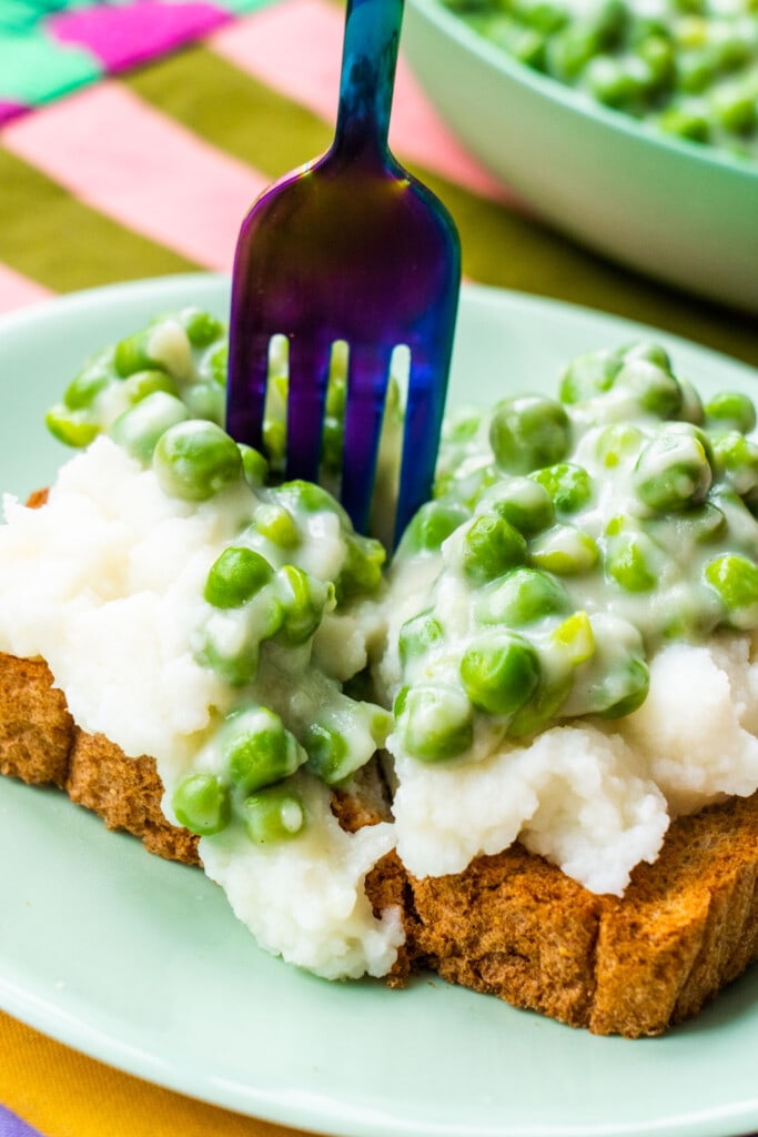 fork cutting a piece of toast with potatoes and peas.