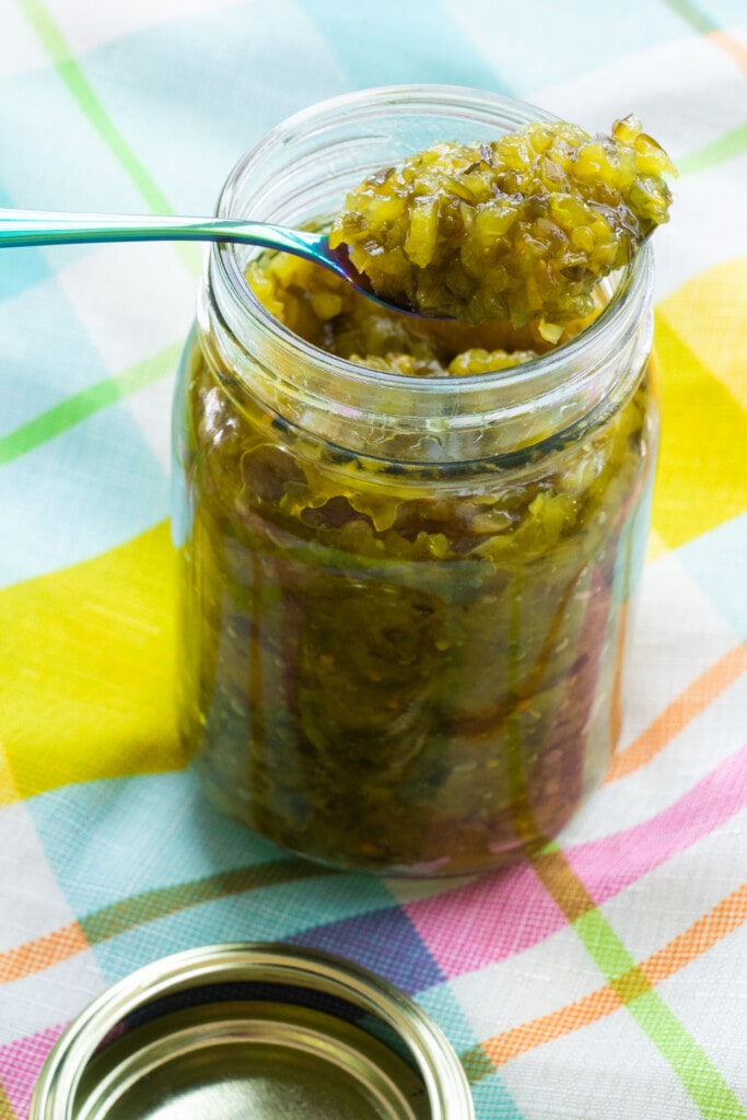 glass jar filled with relish on patterend table cloth.