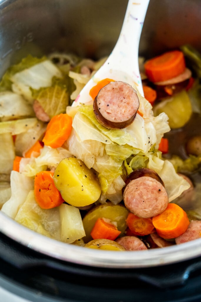 spoon stirring cabbage and kielbasa cooked in instant pot.