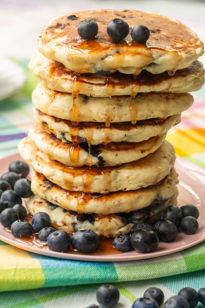 stack of blueberry pancakes on table with maple syrup running down.