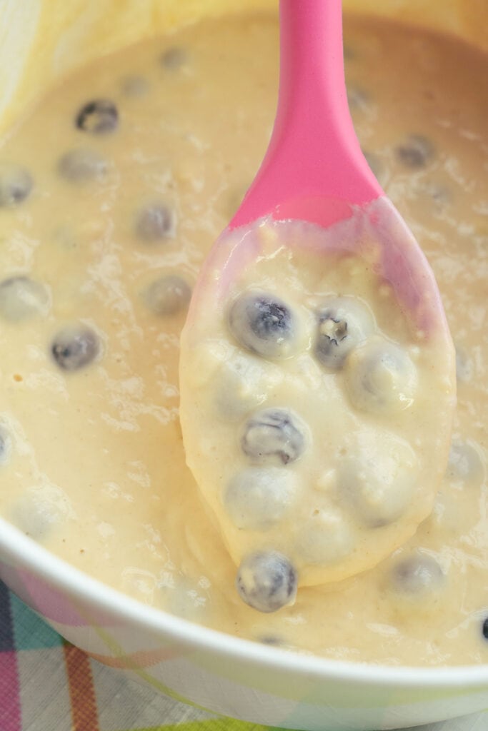pink spoon filled with blueberry pancake batter.