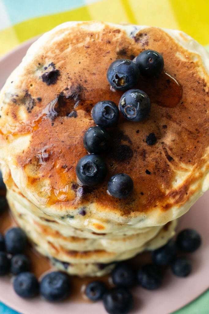closeup of blueberry pancakes with syrup and blueberries on them.