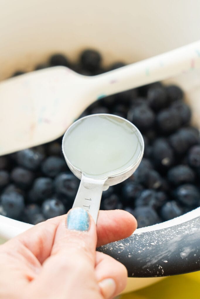 hand measuring lemon juice into bowl with blueberries.