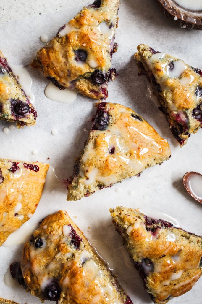 blueberry scones cut up into scone shapes on parchment paper with glaze.