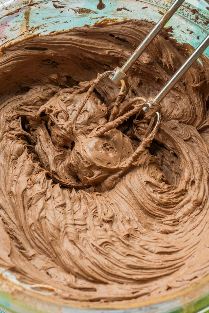 beaters mixing chocolate frosting in bowl. 