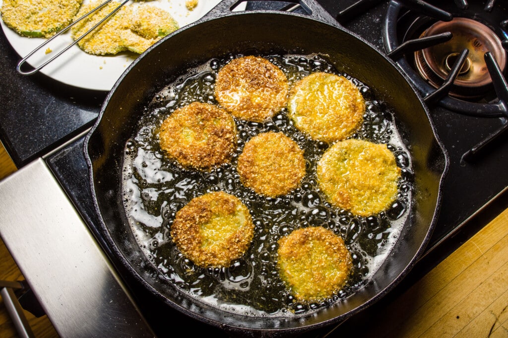 green tomatoes being fried in large skillet. 