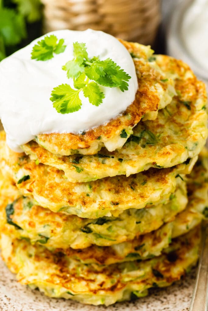 zucchini fritters with sour cream on top of each other on plate.