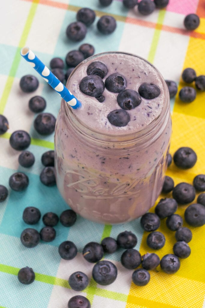 blueberry smoothie in glass cup with blueberries on top.