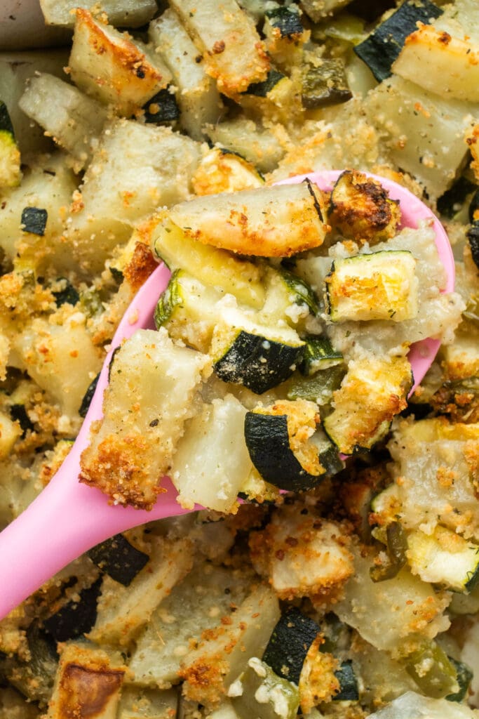 pink spoon serving zucchini potato casserole. 