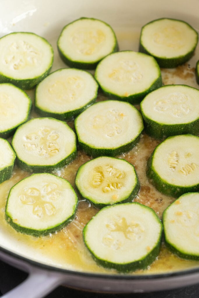 zucchini slices in simmering butter sauce in skillet.
