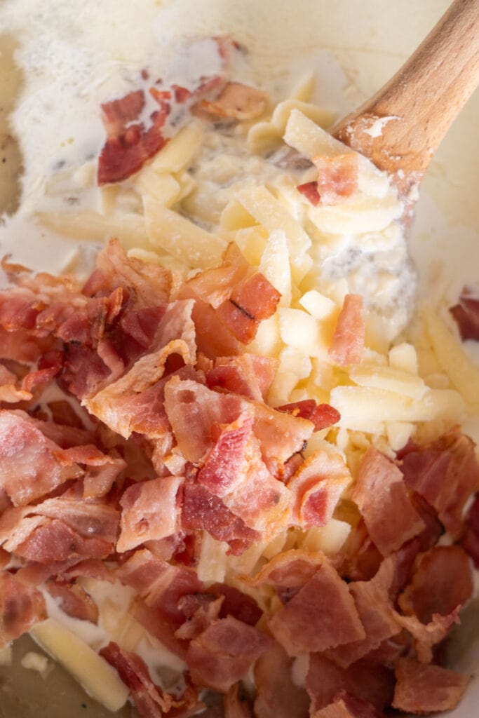 bacon, cheese and sour cream added into slow cooker with spoon mixing it.