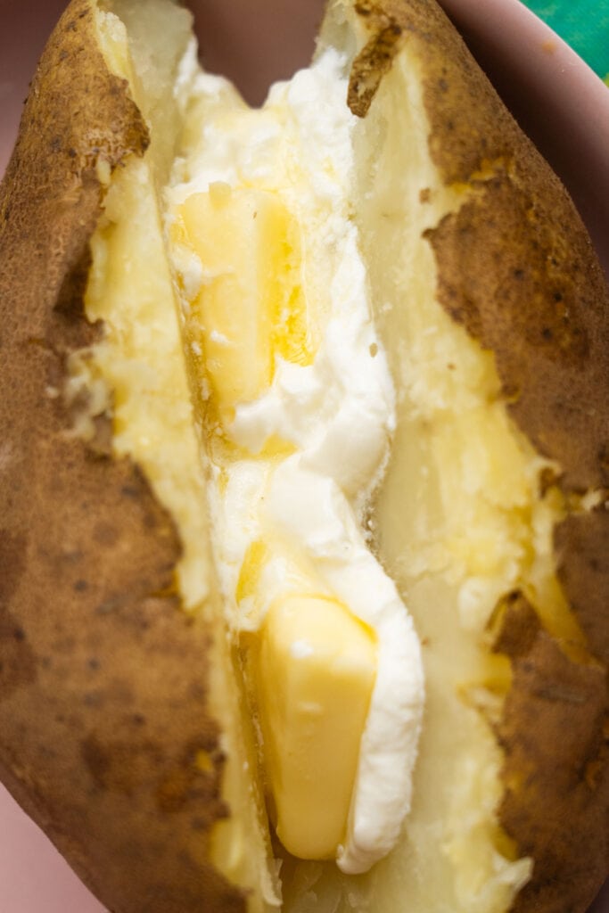closeup of baked potato with melting butter and sour cream.