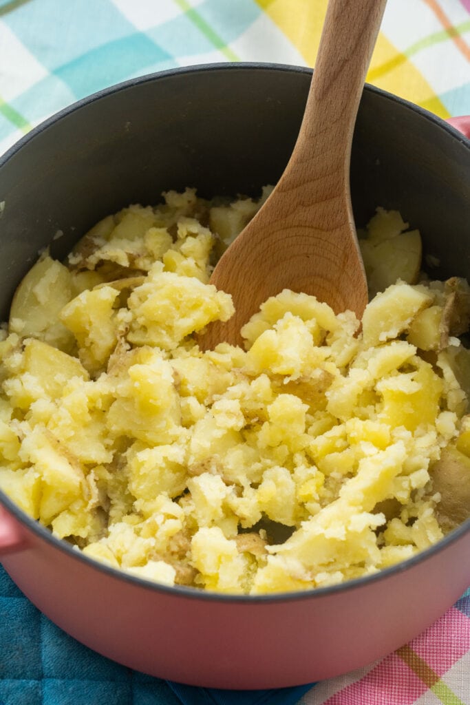 wooden spoon breaking up potatoes in pot.