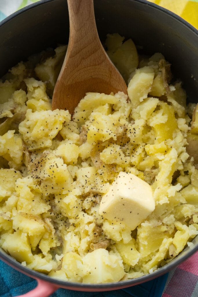 milk, butter and salt and pepper being added into pot with potatoes.