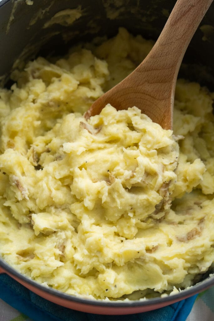 spoon lifting out chunky mashed potatoes out of pot.