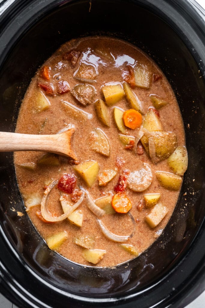 peanut butter and potato stew in crockpot with wooden spoon stirring.