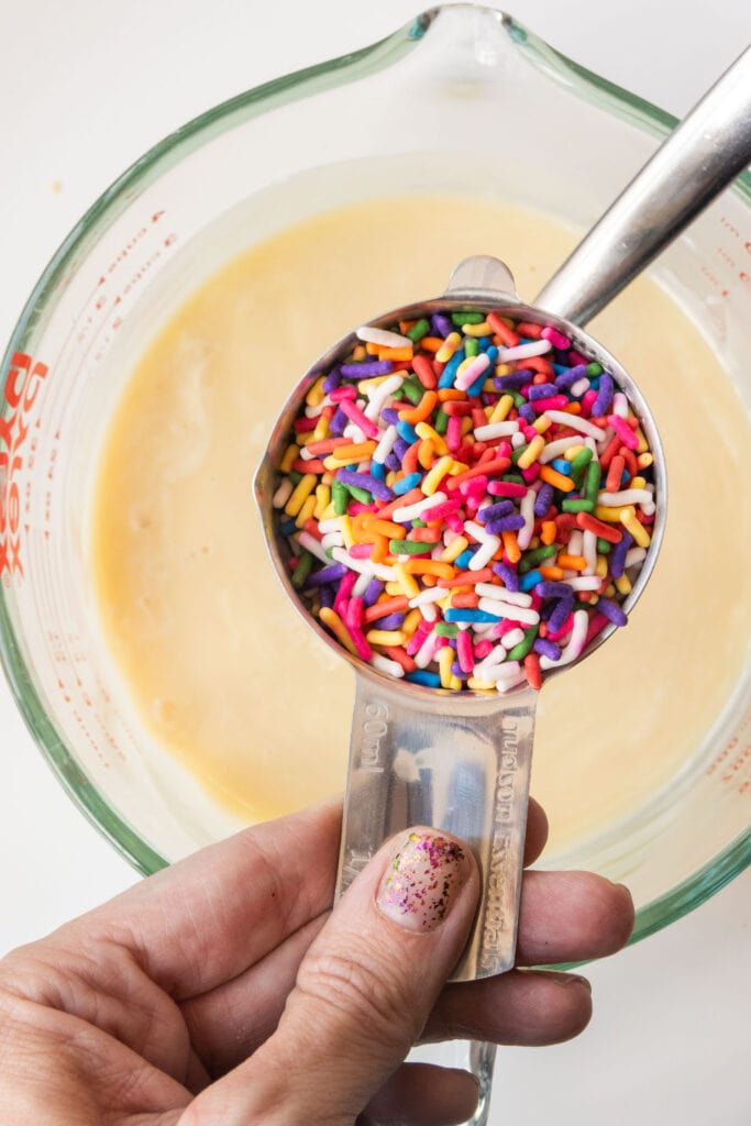 hand holding measuring cup with rainbow sprinkles.