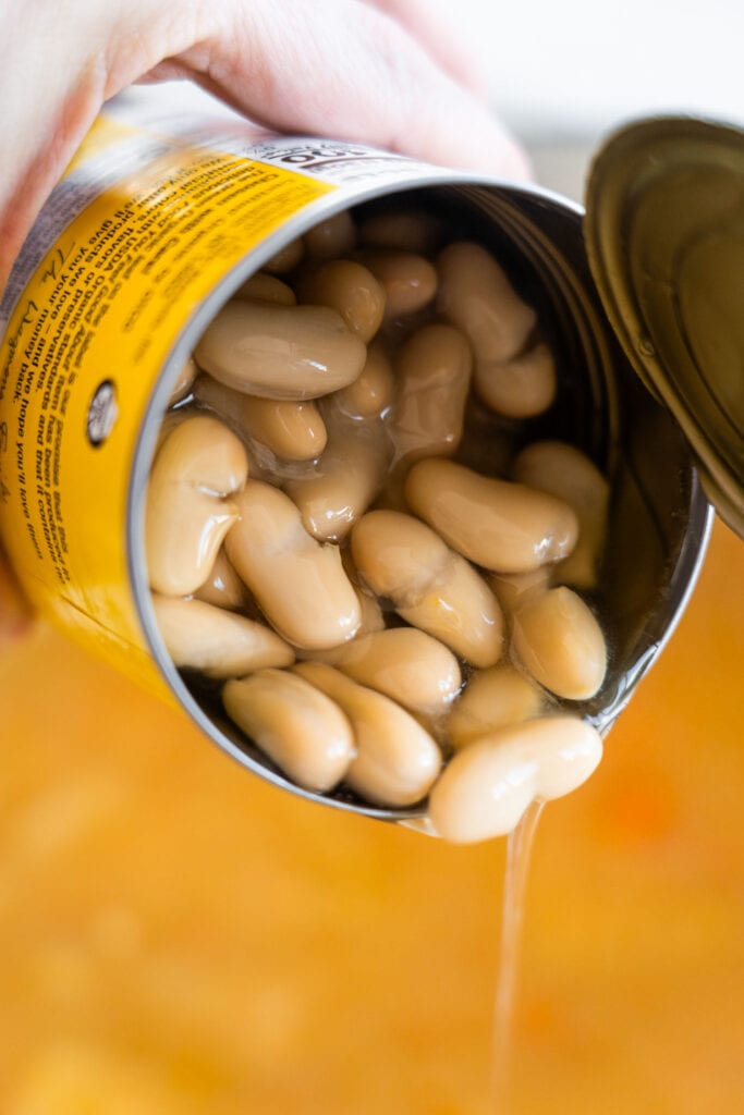 white beans being added into the pot straight from the can.