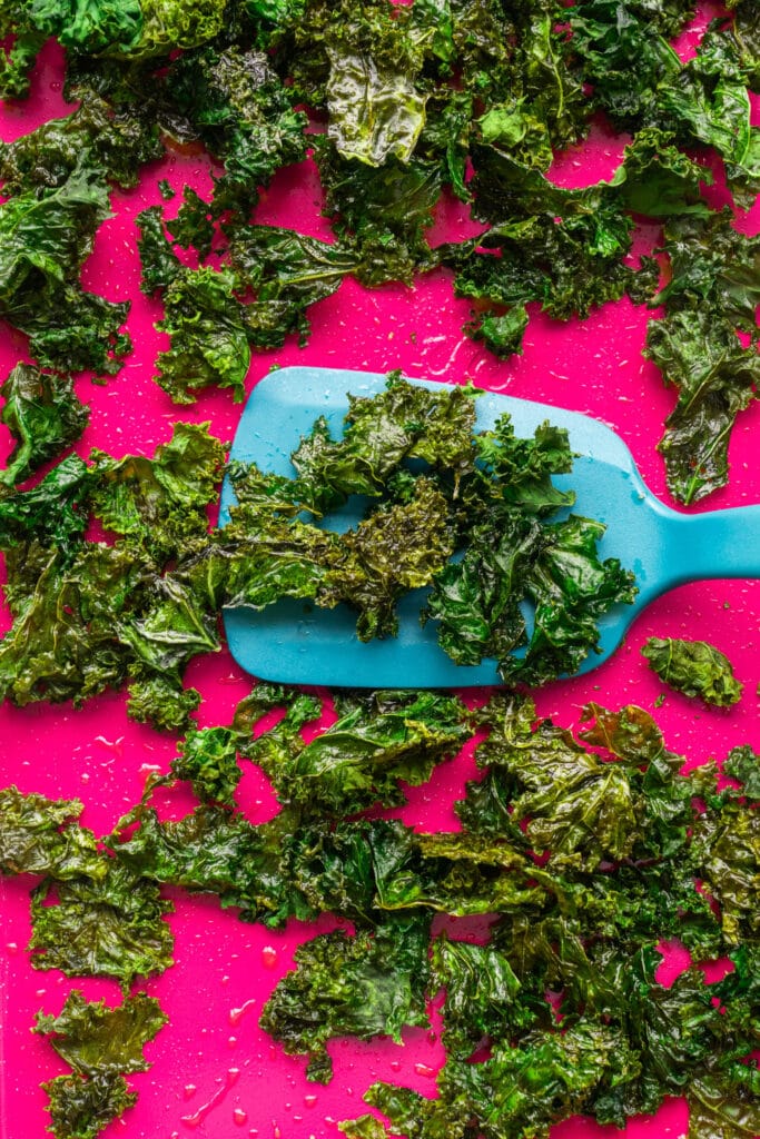 blue spatula lifting out kale chips from baking sheet.