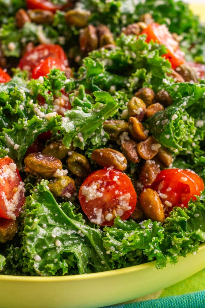closeup of kale salad with parmesan cheese, cherry tomatoes and pistachios.