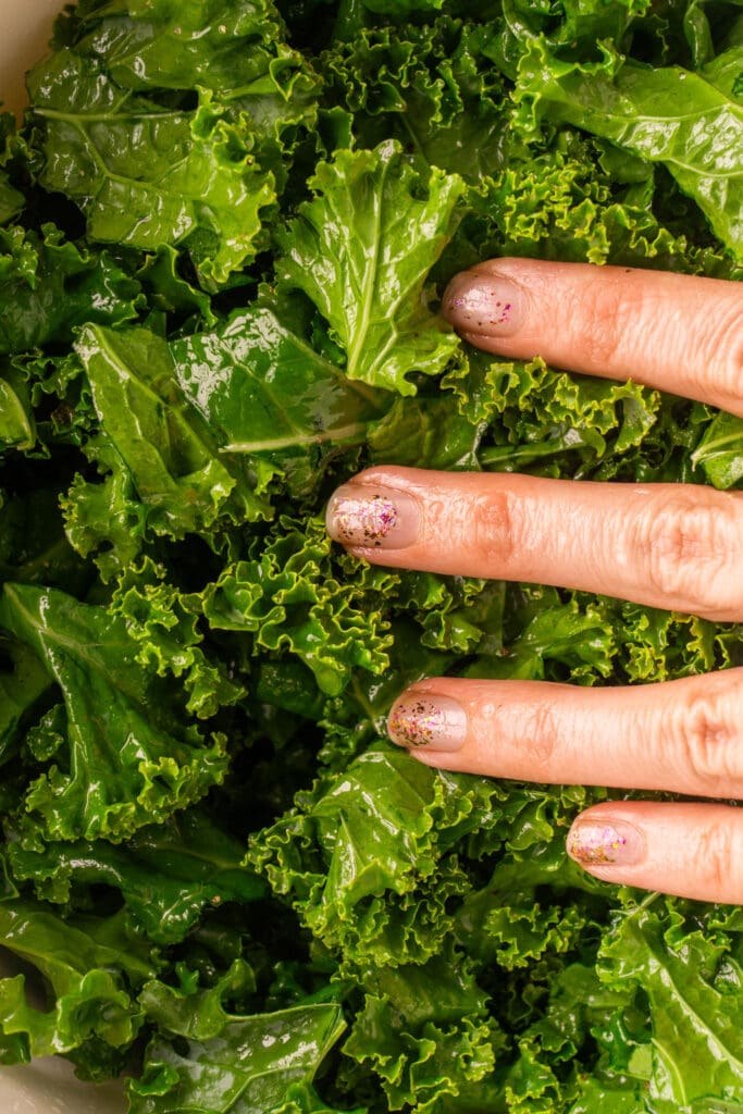 hand massaging kale with olive oil in bowl. 