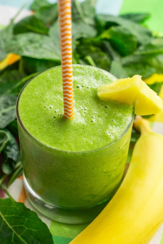 kale smoothie in glass cup with straw in it.