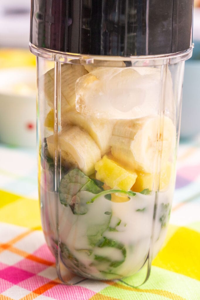 kale, pineapple, bananas, ice cubes and almond milk in blender cup.