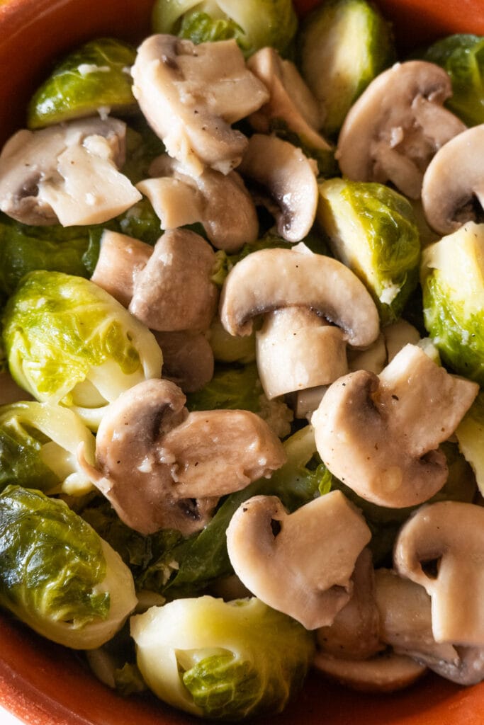 closeup of buttery brussels sprouts and mushrooms in a red bowl. 