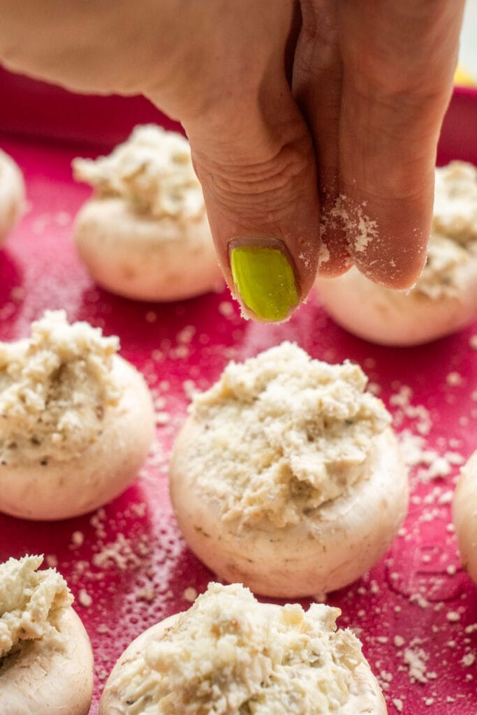 hand sprinkling parmesan cheese on top of stuffed mushrooms.