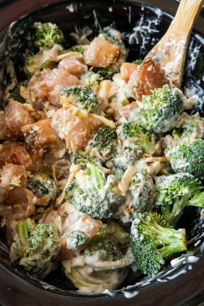 spoon stirring chicken and broccoli in slow cooker.