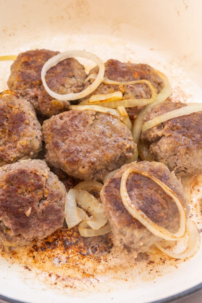 browned hamburger steaks in skillet with onions.