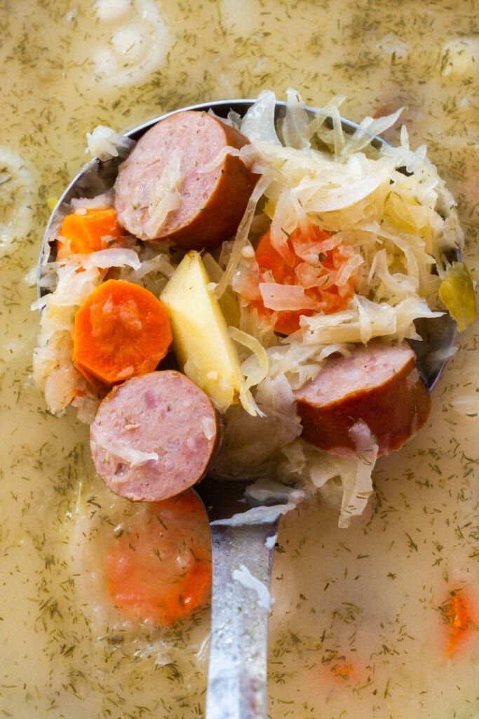 spoon filled with sauerkraut soup with sausage and vegetables. 