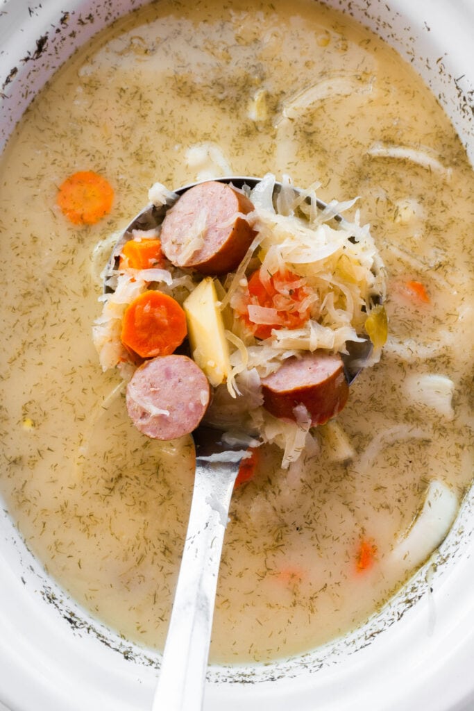 spoon serving sauerkraut soup in slow cooker.